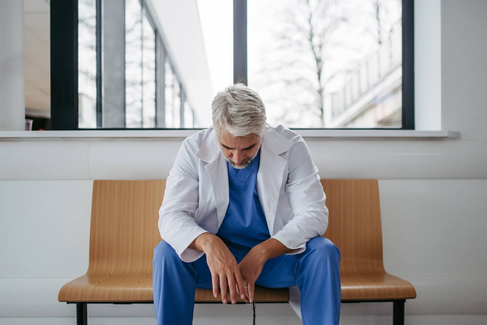 A stressed physician sitting at a desk surrounded by electronic health records, highlighting excessive EHR workload.